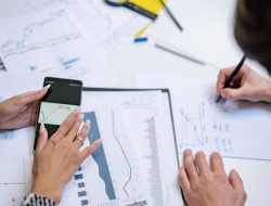 Pandangan dari atas orang-orang yang menganalisis grafik dan data keuangan dengan ponsel pintar dan dokumen.