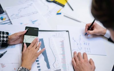 Pandangan dari atas orang-orang yang menganalisis grafik dan data keuangan dengan ponsel pintar dan dokumen.
