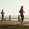 Orang-orang berlari dan berjalan di sepanjang jalan setapak pantai saat matahari terbenam, mewujudkan gaya hidup aktif.