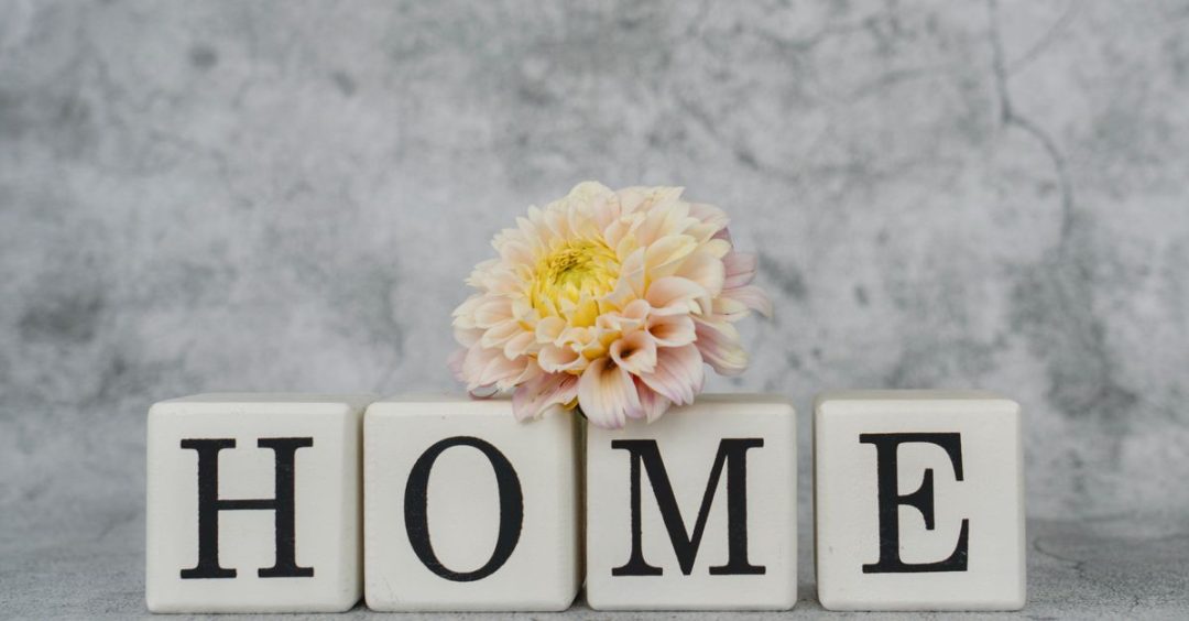 Dekorasi rumah yang stylish menampilkan huruf-huruf yang mengeja 'HOME' dengan aksen dahlia yang lembut untuk menciptakan suasana yang nyaman.
